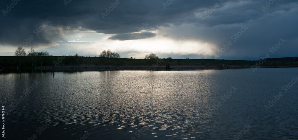 Panoramic view on dramatic stormy dark sky over the pond at spring, almost monochrome,siluette