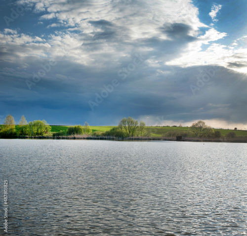 lake before the storm and beautifully lit trees and fields in spring. weather...