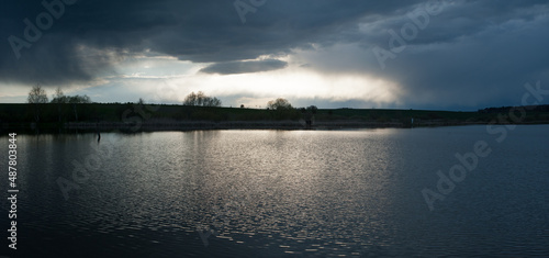 Panoramic view on dramatic stormy dark sky over the pond at spring, almost mo...