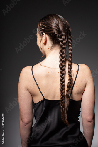 Turned back young european woman with two braids isolated on dark grey in total black outfit