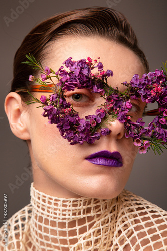 Young woman with eye mask made of small flowers with purple lips portrait