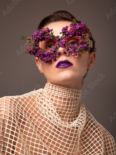 Woman with eye mask made of small flowers with purple lips portrait isolated on grey brown