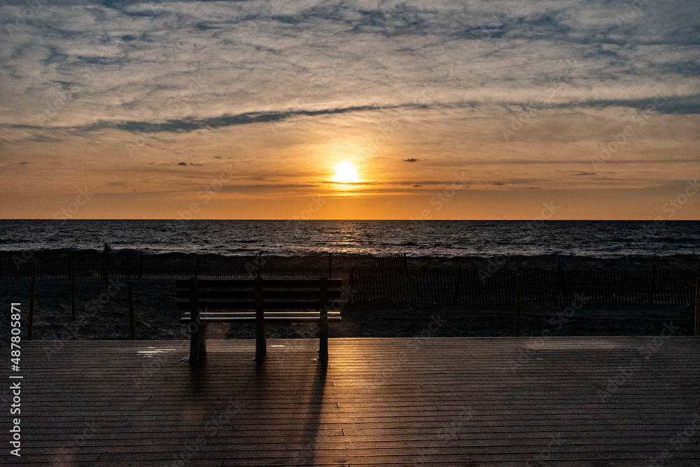 Sunrise and a bench on the boardwalk by the beach