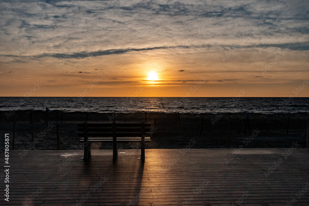 Obraz premium Sunrise and a bench on the boardwalk by the beach