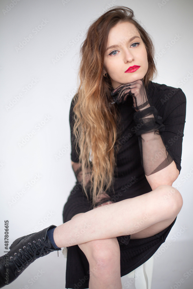 Fototapeta premium White young european woman sitting in total black isolated on grey