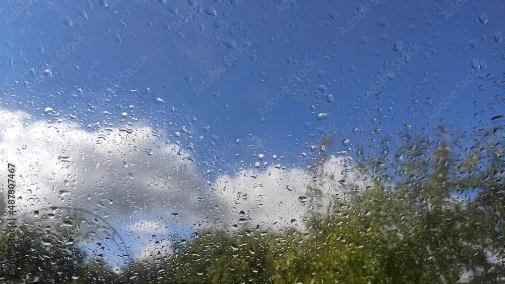Drop spreading on the glass against the background of trees and a blue sky with clouds Drop spreading on the glass against the background of trees and a blue sky with clouds