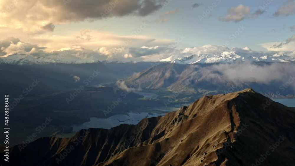 Sunlight shining on the mountains during sunrise, beautiful hills with snow above a valley with a river running through. Clouds in the sky. Panning aerial drone shot. Sunlight shining on the mountains during sunrise, beautiful hills with snow above a valley with a river running through. Clouds in the sky. Panning aerial drone shot.
