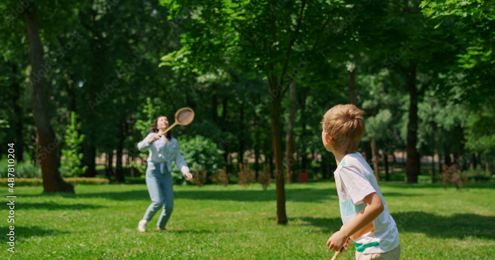 Active boy playing badminton with mother back view. Sport in family life concept