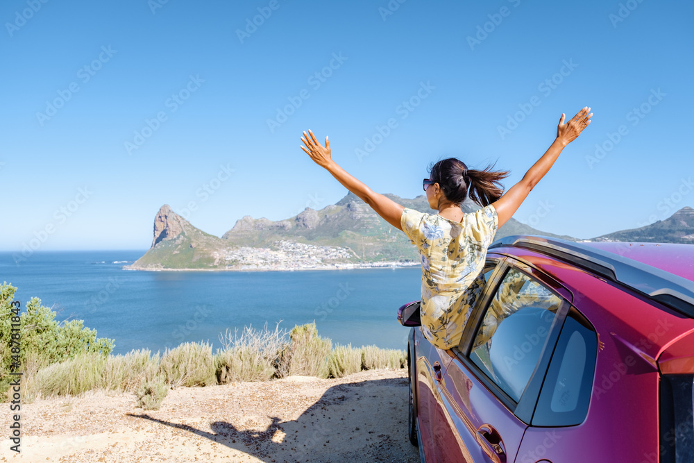 Fototapeta premium woman outside car window road trip with hands up, car at Chapmans Peak Drive in Cape Town South Africa looking out over the ocean. 