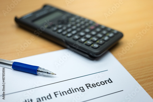 A ball pen is placed record document paper with blurred background of calculator on wooden table. Business and finance workplace scene photo. Close-up and selective focus at pen nib.