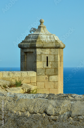 A seagull sits on a castle tower of castillo de Santa Bárbara in Alicante overlooking the Mediterranean Sea under clear blue sky