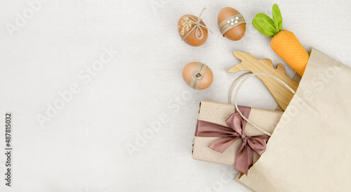 Eggs, carrots and a wooden hare in a kraft bag.on a light wide background.Minimalistic decor for Easter. Spring Religious holiday.The concept of a holiday and shopping for Easter.
