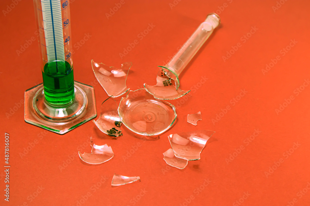 Broken laboratory glass. Green liquid in measuring glass. Failed lab