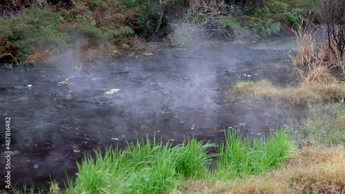 Geothermic hot water river gently flowing downstream with clouds of steam and mist drifting from waters surface in unusual geothermal landscape. photo