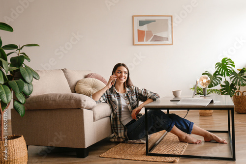 Portrait of young brunette woman wearing flannel shirt talking on the phone and smiling. Joyful female having fun phone call by the workspace of her home office area. Background, copy space, close up. © Evrymmnt