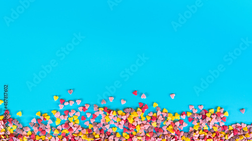 flatlay mockup made of multi-colored sugar hearts on a turquoise background in the the shape of the strip at the bottom of the frame