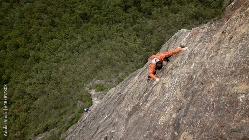 Rock climber scaling a huge steep mountain above a green valley. He slowly struggles and makes his way up the mountain face. photo