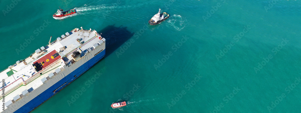 Aerial drone ultra wide photo of large car carrier ro ro vessel guided by tug boats to depart from logistics terminal port