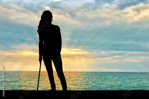 A silhouette of a woman supports herself with a crutch