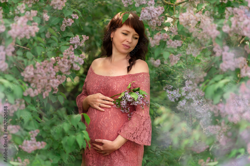 A young pregnant woman stands in the lilac bushes. A young pregnant woman stands in the lilac bushes.