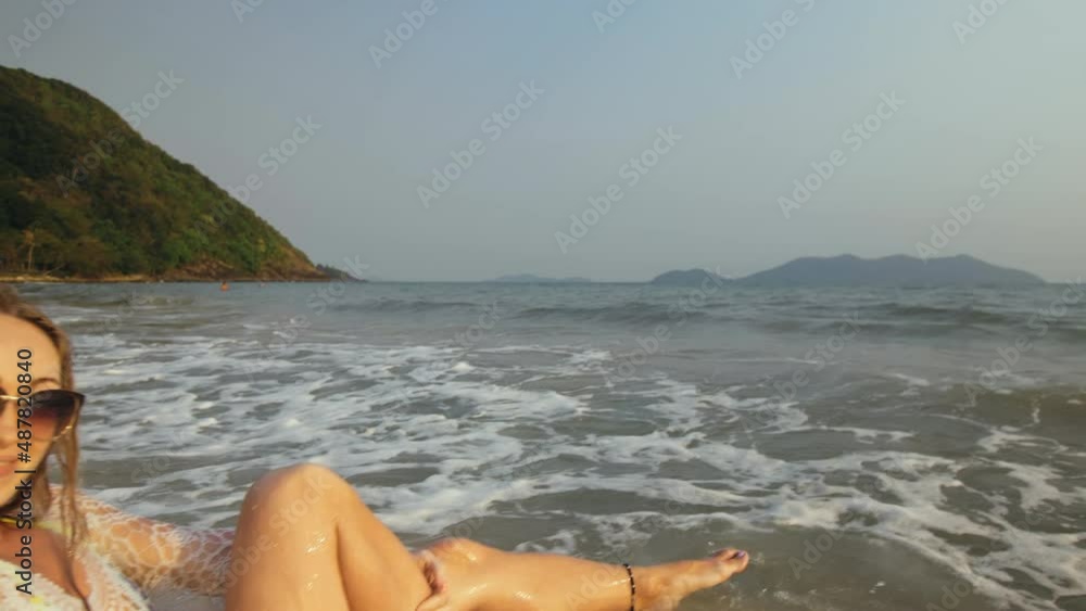 Crazy Woman in a White Tunic on the Beach, near the Stormy Sea. Cheerful Funny Charming Blonde with Wet Curly Hair, in Sunglasses. Smiling Happy Girl Tourist Lies in the Water, has Fun. Chill Travel Crazy Woman in a White Tunic on the Beach, near the Stormy Sea. Cheerful Funny Charming Blonde with Wet Curly Hair, in Sunglasses. Smiling Happy Girl Tourist Lies in the Water, has Fun. Chill Travel