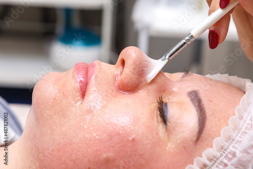 A cosmetologist performs spa treatments with the face of a young pretty woman.
