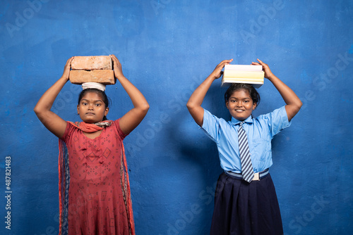 Fototapeta Two girl kids with books and bricks on each other head looking at camera - concept poverty and conflict or necessary between education and child labour