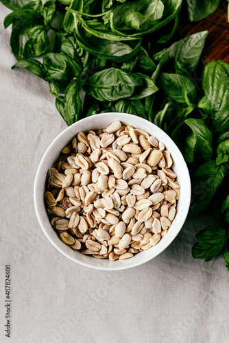 Photo of a fresh healthy ingridients like green basil, fresh garlic, roast nut, parmegiano cheese to make homemade pesto sauce on a wooden desk indoors daylight photo