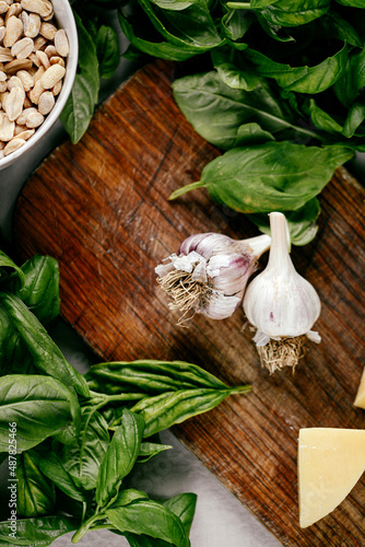 Photo of a fresh healthy ingridients like green basil, fresh garlic, roast nut, parmegiano cheese to make homemade pesto sauce on a wooden desk indoors daylight photo