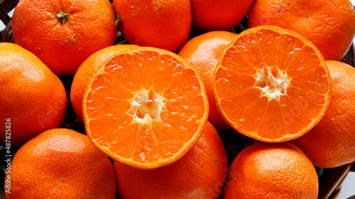 Foto close up of a halves ripe clementine oranges set on whole orange fruit in wood basket background