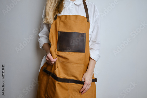 A woman in a kitchen apron. Chef work in the cuisine. Cook in uniform, protection apparel. Job in food service. Professional culinary. Camel fabric apron, casual clothing. Handsome baker posing 