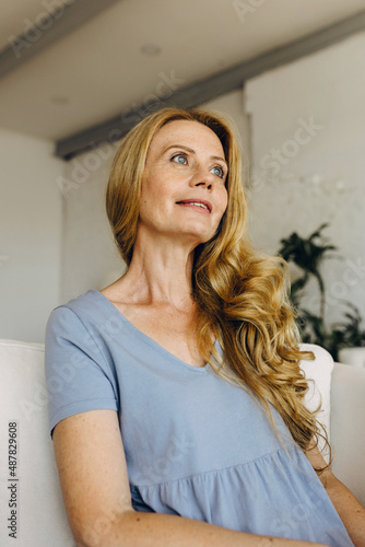 Horizontal close-up picture of attractive woman of 50s having pensive look  dreaming about little house at seashores  vacations and traveling abroad  wearing good long wavy hair and grey-blue clothes