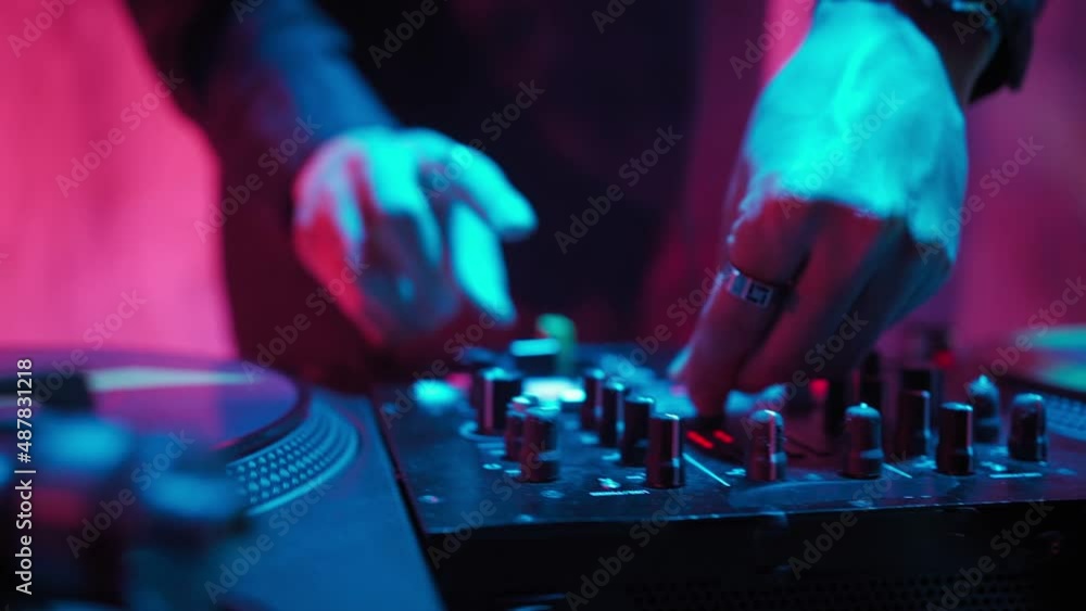 Close-up Modern DJ of Asian Appearance Performs a Music Track in Neon Lighting. Working at the Mixer, a Man Puts on Records, Sound Tracks, Individual Sounds and Makes a Mix Out of Them. Close-up Modern DJ of Asian Appearance Performs a Music Track in Neon Lighting. Working at the Mixer, a Man Puts on Records, Sound Tracks, Individual Sounds and Makes a Mix Out of Them.