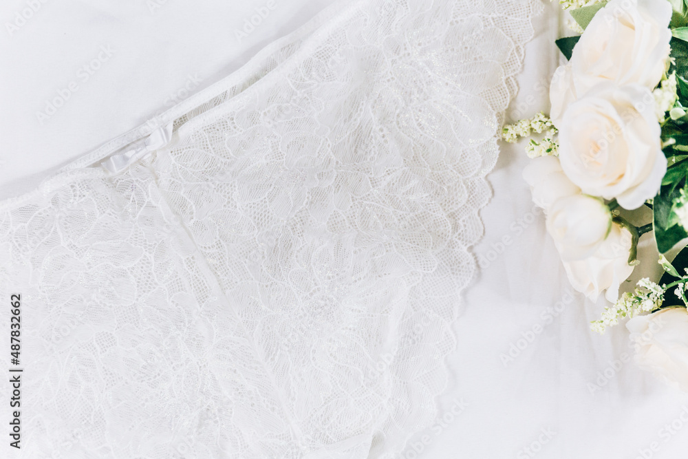 Fototapeta premium White women lace underlace and flowers on the bed. Top view, flat lay 