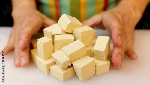 a person in the kitchen wearing a green apron prepares the meal by cutting a block of tofu into squares