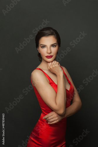 Attractive fashion model woman with makeup wearing red silky dress posing on black background