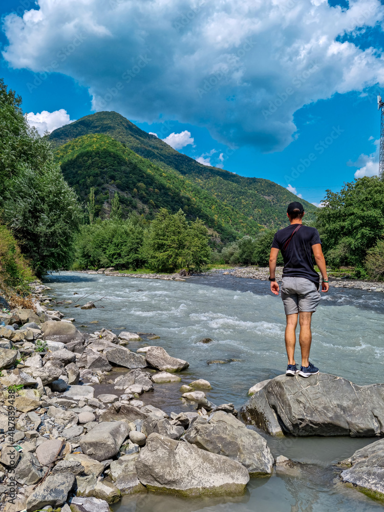 A man watching the black (shavi) Aragvi river and white (tetri) Aragvi river in Georgia that do not mix up. Unmixed waters. Confluence of rivers, Caucasus Mountains. Georgian military Highway.