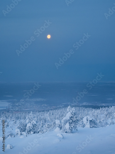 Red full cold moon over a snow-covered slope. Winter polar landscape. Cold winter weather. Harsh northern climate. Minimalistic vertical view.