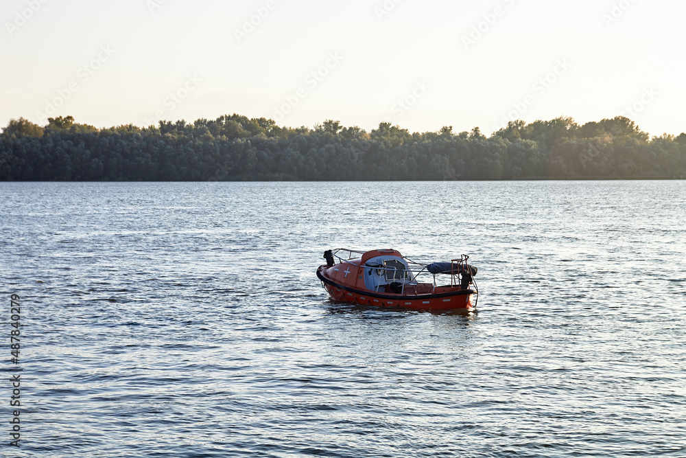 An empty lost orange lifeboat floats down the river An empty lost orange lifeboat floats down the river