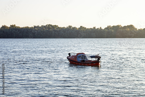 An empty lost orange lifeboat floats down the river