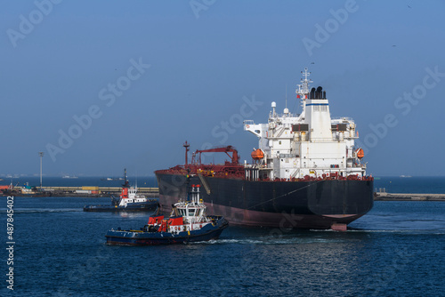 Cargo vessel going to sea from port with tug assistance. Bulk carrier. Dry cargo ship.