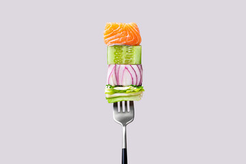 Close-up of fork with food on it: delicious fillet salmon, cucumber, onion, green salad on gray color background. Concept of healthy diet and clean eating with fish and vegetables, balanced nutrition