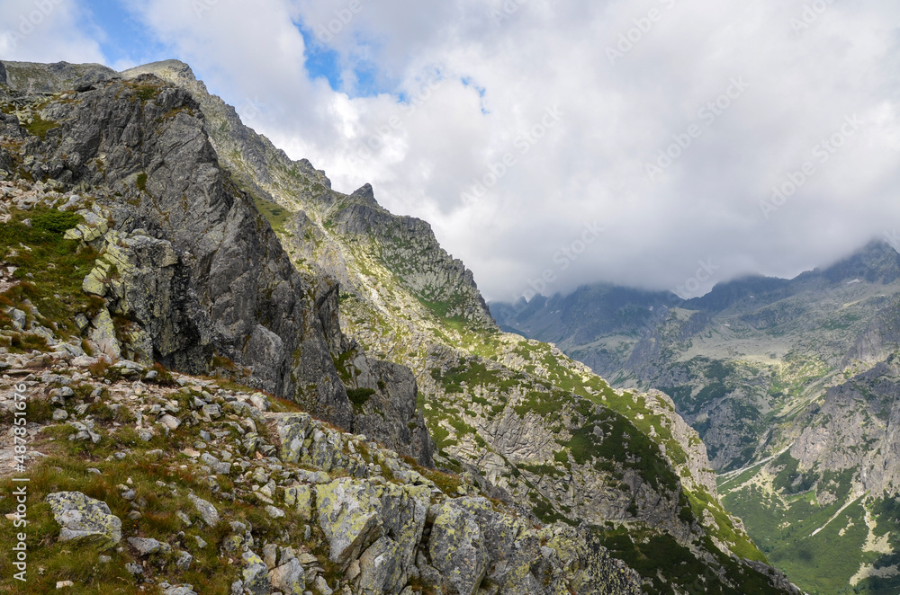 View of sharp green mountain and rock landscape with low clouds over the peaks in High Tatras, Slovakia