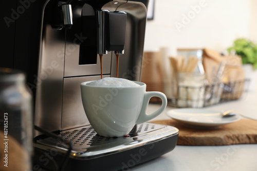 Modern coffee machine making cappuccino in kitchen, space for text
