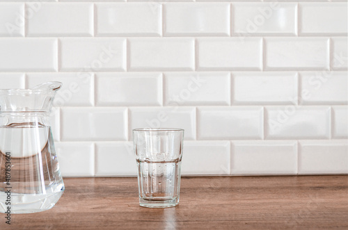 An empty glass and a jug of water stand in the kitchen