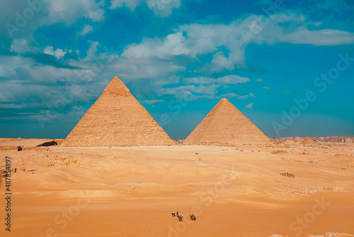 Amazing wide view of the great pyramids of giza. Desert dunes everywhere  people on camels and horses riding around them