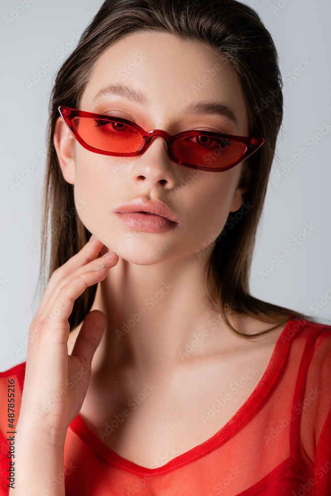 young model in red stylish sunglasses isolated on grey.