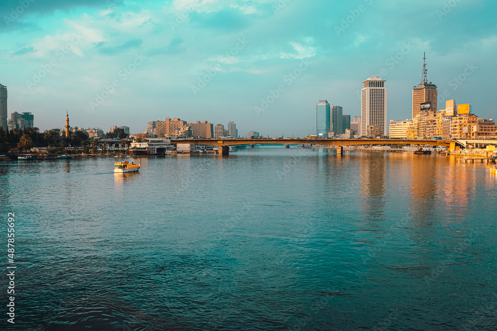Naklejka premium Cairo Egypt December 2021 View of the amazing Nile river at sunrise, boats anchored on the shores. Bright blue river and sky colors. Skyscrappers in the distance