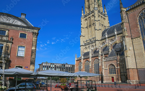 Arnhem, Netherlands - July 9. 2021: View over square (Kerkplein) on restaurant with people sitting outdoor and gothic church tower from 14th century against blue summer sky