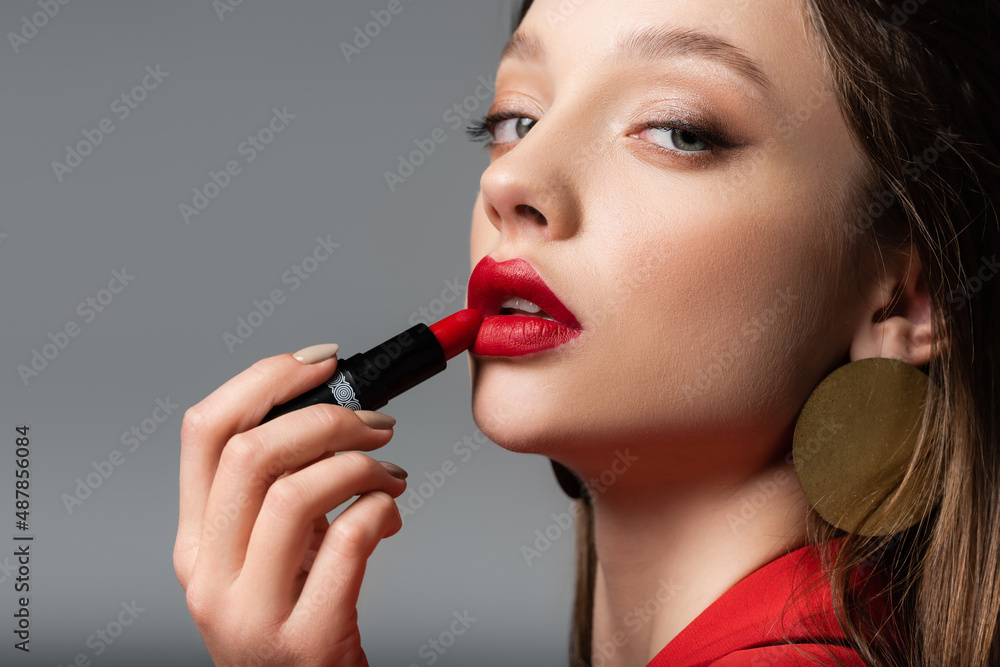 close up of young woman applying red lipstick isolated on grey. close up of young woman applying red lipstick isolated on grey.